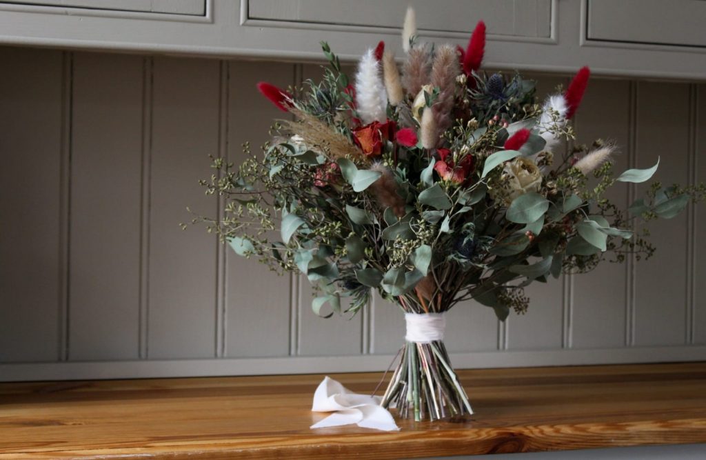Seasonal mixed dried wedding bouquet with dried grasses, greenery and orange and cream accents by The Flowers of May, Cornwall florist