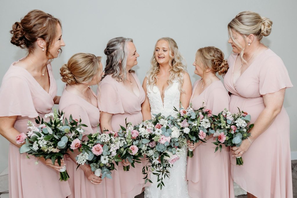 Bride and bridesmaids holding white and pale pink bouquets by The Flowers of May