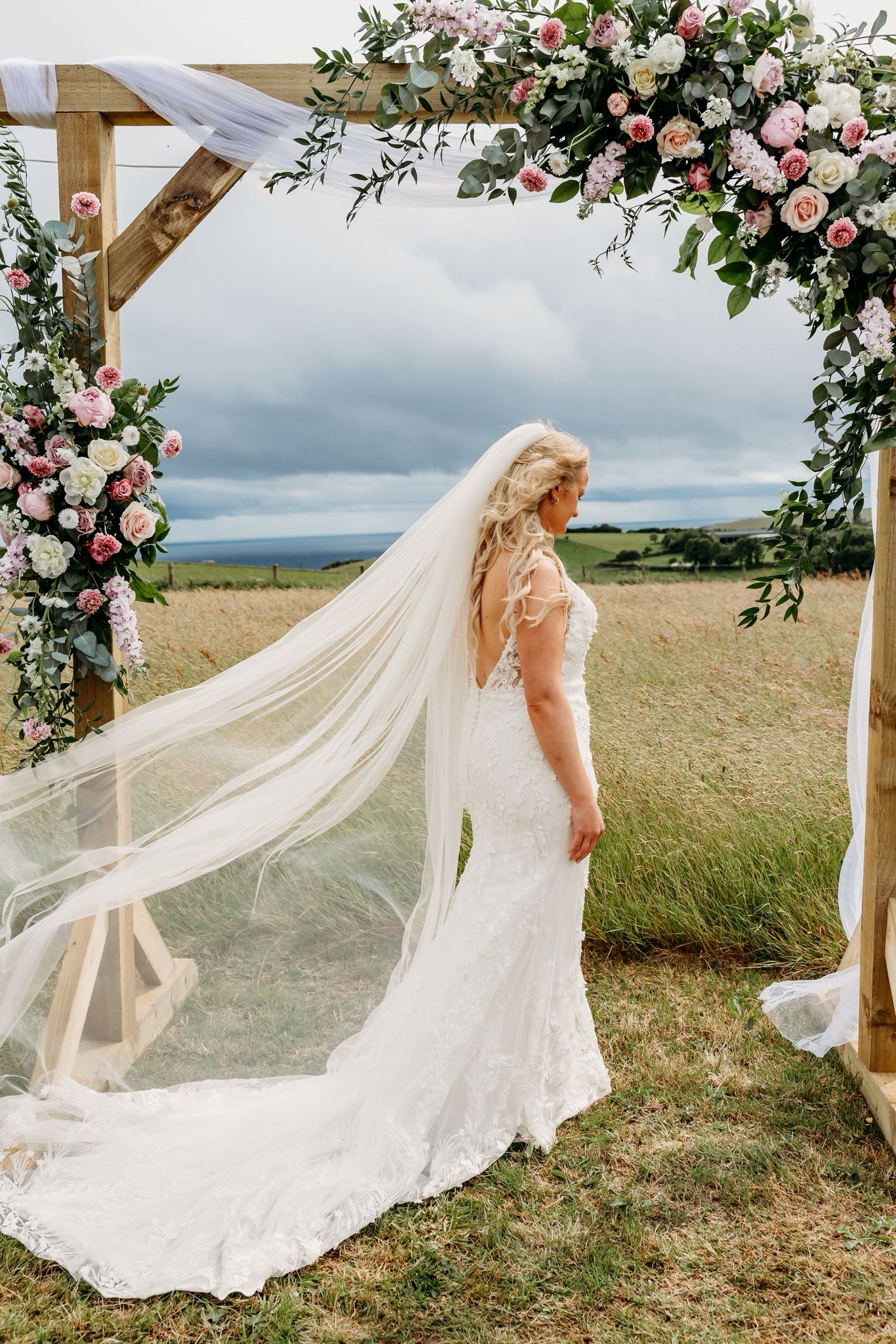 Pale pinks and white floral archway with bride stood under archway by The flowers of May