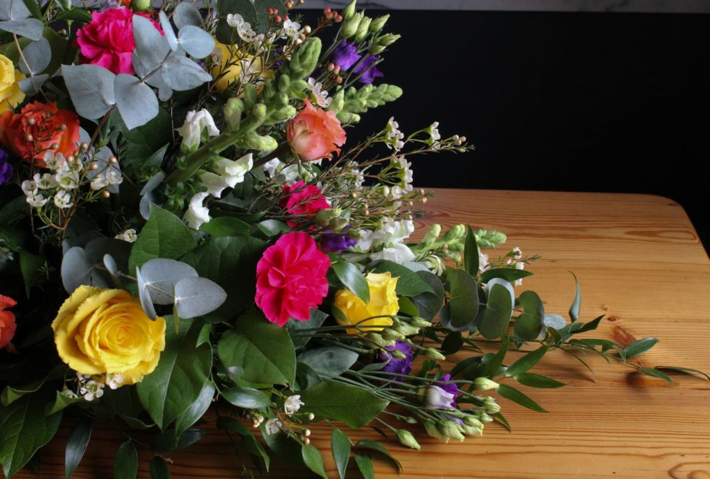 Brightly coloured flowers and lush greenery in a casket spray by The Flowers of May